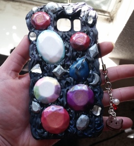 Cam O Chan's friend ordered a custom case based on the TV show StevenUniverse. He wanted it to be outer space themed and incorporate his favorite characters. The large clay gemstones represent a few of the characters. The black frosting is coated with blue and purple shimmer powder, but that didn't come out very well in the picture. Lastly, there is a dangly charm of the lovable character Cookie Cat. 